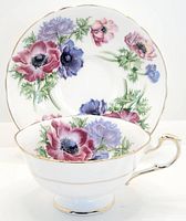 Front view of vintage tea cup and saucer with colorful floral pattern and gold trim on white fine bone china.