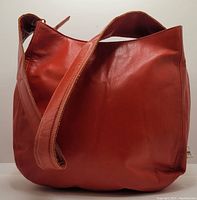 Front and side view of burnt orange leather handbag showing padded strap and smooth leather body.