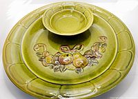 Top-side view of the green glazed round ceramic platter with attached dip bowl and embossed fruit decoration.
