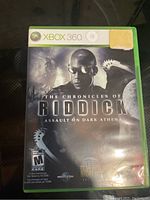 Front cover of The Chronicles of Riddick: Assault on Dark Athena Xbox 360 game case. Shows artwork of main character and rating.