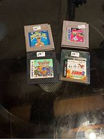 Four GameBoy game cartridges arranged on a surface. Titles visible: Navy Blue, Daisy World, and two Japanese games. Cartridge labels show signs of wear.