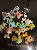 Top view of 15 assorted Littlest Pet Shop animal figures laid out on a black surface. Figures include various species such as dogs, cats, birds, and other small animals, each with characteristic large eyes and detailed paint.