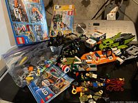 Wide view of the Lego lot on a black surface including multiple vehicles, minifigures, loose pieces, and boxes.