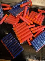 Photo showing a collection of red and blue off-brand foam darts with orange tips, arranged loosely on a dark surface.
