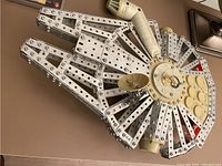 Metallic Meccano construction model representing the Millennium Falcon from Star Wars, showing the detailed assembly with beams, riveted strips, and circular plates.