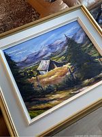 Framed painting showing a mountain cabin with trees and mountains, signed by Christine Normandin.