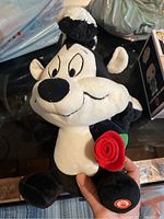 Plush toy of Peppy La Pew, the cartoon skunk holding a red rose.