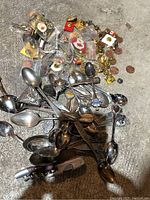 Photo showing a mixed lot on a grey surface with various metal souvenir spoons and a large collection of collectible pins mainly with Canadian themed designs including maple leaves