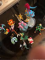 Top-down photo of various Pokémon, Digimon, Hello Kitty, and other collectible figures on a dark reflective surface.