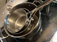 Stack of three stainless steel pots with long handles visible from above and side view on stove.