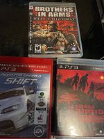 Photo showing three PlayStation 3 game cases: Brothers in Arms: Hell's Highway, Need for Speed Shift, and Dead Island Riptide Special Edition.