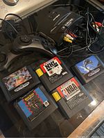 Aftermarket Sega Genesis system with connected AV cables and five Sega Genesis game cartridges laid out.