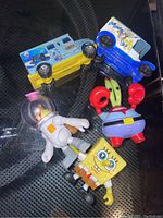 Photo showing three SpongeBob character figures and two toy cars upside down on a surface.