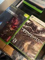 Photo of two Terminator video games in their cases for Xbox and Xbox 360 systems, showing front covers and minor wear.