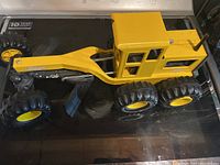 Top and side view of a large yellow Tonka toy plow truck with a die cast cabin and plastic wheels and plow parts resting on a black surface.