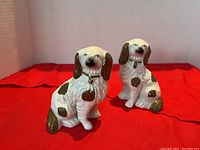 Pair of matching ceramic dog figurines on red fabric background.