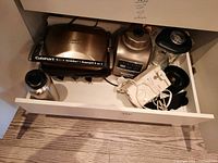 Drawer with KitchenAid blender with glass jar and lid, Cuisinart Griddler, electric can opener, and mug.