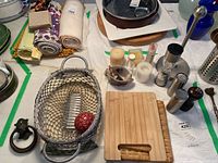Assorted kitchen implements including trivets, salt and pepper shakers, a pepper mill, paper towel holder, candles, and decorative items arrayed on table.