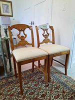 Pair of matching wood frame side chairs with upholstered seats placed on patterned rug. Visible decorative back design and beige striped fabric upholstery.