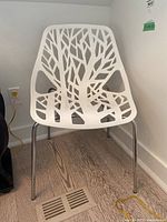 Side view of one white plastic chair with chrome metal legs on wooden floor near a floor vent.