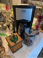 Photo showing the entire lot: DeLonghi coffee maker, manual coffee grinder with wooden base and green top, and Schott Duran French press.