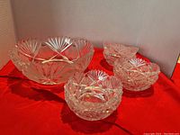 Overall view of one large crystal bowl and six smaller bowls arranged on a red cloth background showing the cut crystal patterns and sizes.