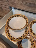 Photo of dinner bowls and plates with ornate black and gold floral rims stacked in a drawer.