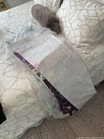 Drapes folded and wrapped in plastic on bed showing partial floral pattern and lining.
