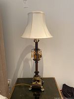 Full view of one table lamp showing fabric shade, dark brown pedestal base, gold accents, and amber bead decoration