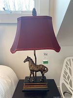 Full view of one lamp showing horse figurine base, stem, finial and burgundy shade