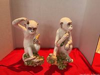 Both monkey figurines side by side on red cloth background