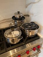 Photo of assorted stainless steel pots and pans including covered saucepan, mixing bowls and egg poacher on stove