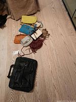 Photo of eight ladies' purses lying on wooden floor showing various colors and styles including crossbody and fringe details.