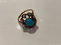 Top-down view of ring showing turquoise-colored cabochon and surrounding clear stones with black enamel