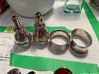 Salt and pepper shakers with two sterling silver napkin rings side by side on a white surface with green tape.