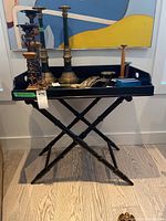 Full view of the black folding side table with Halloween candle holders and decorative items placed on top. Table legs crossed forming an X shape with turned spindle detailing.