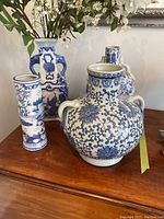 Overview of all four blue and white porcelain vases on wooden surface, including faux flowers in the rectangular vase.