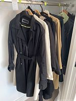 Multiple women's coats hung in a row showing colors black, cream, tan, navy, and olive green.