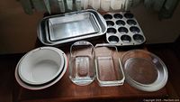Photo showing aluminum oblong pans, muffin tin, Pyrex loaf pans, Pyrex pie plates, and ceramic coated pans arranged on a wooden surface.