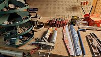 Overview of workbench containing green tiered rotating tool carriers filled with small parts and hardware items, caulking guns, screwdrivers, clamps, a crowbar, and a 36-inch level.