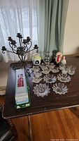 Overall assortment of vintage candle holders on a wooden table including metal candelabra, various glass candle holders, ceramic ducks, and boxed clear glass tapers.