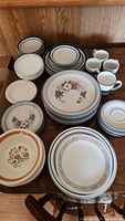 Full view of assorted dinnerware including plates, bowls, mugs, and saucers arranged on wood surface.