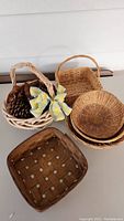 Overview of all baskets including the light-colored handled basket with bow, square basket, and several round baskets