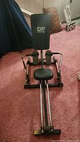 Photo showing front view of the DP rowing machine including sliding seat, foot pedals with straps, and push bars set on dual metal rails.
