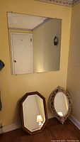 Elevated view of oak framed mirror, vintage oval gilt frame mirror, and large frameless mirror hung on wall
