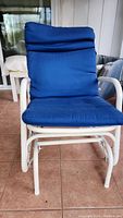 Front view of the outdoor slider rocker chair showing the padded blue seat and back cushions and white metal frame.