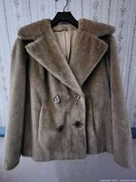 Front detailed photo of light brown vintage fur coat showing double breasted large button style, wide collar, and bracelet length sleeves.