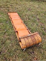 Top view of wooden toboggan laid on grass showing curved front and attached orange vinyl pad.