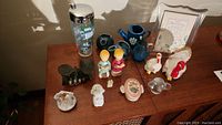 Collection of assorted figurines, salt and pepper shakers, cocktail shaker, and musical photo frame on wooden surface