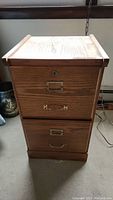 Front view of wooden file cabinet showing two drawers with brass hardware, label holders, and keyhole on top drawer.
